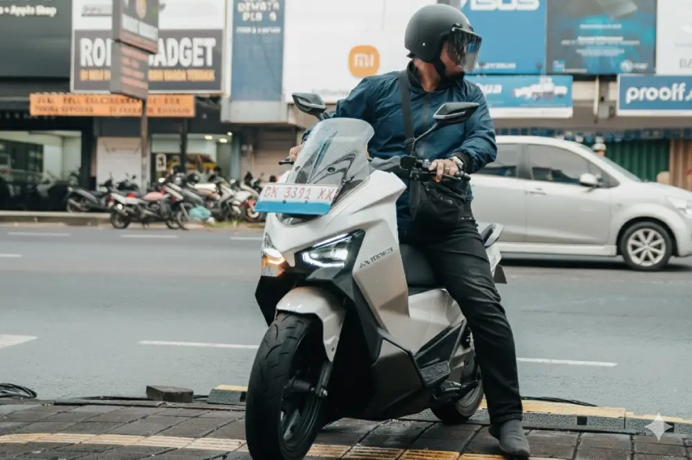 Seorang pria pengendara motor dengan helm di atas skuter matic elektrik Maka Cavalry berwarna putih dari Maka Motors Bali yang berhenti di jalanan perkotaan.