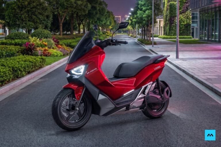 Sepeda motor listrik Maka Cavalry berwarna merah metalik yang terparkir di jalanan aspal modern saat suasana senja.