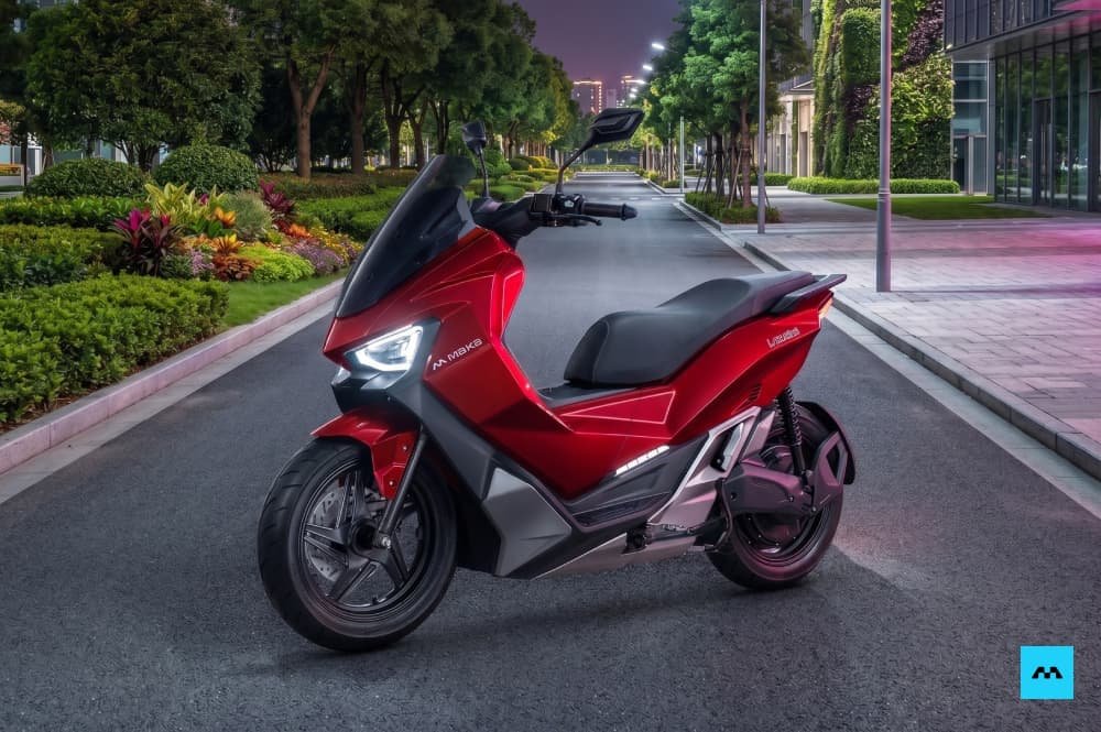 Sepeda motor listrik Maka Cavalry berwarna merah metalik yang terparkir di jalanan aspal modern saat suasana senja.